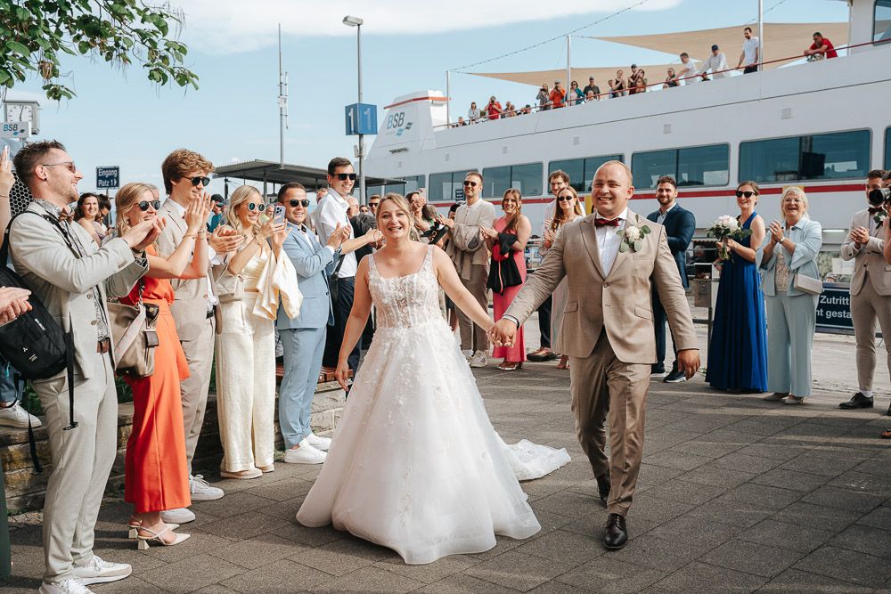 A wedding party dances together on an outdoor pavilion or deck during a summer celebration.