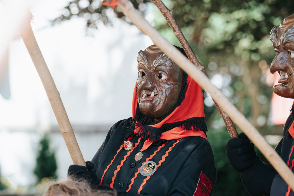 Someone wearing a detailed wolf mask and red trimmed black costume during what appears to be a theatrical performance.