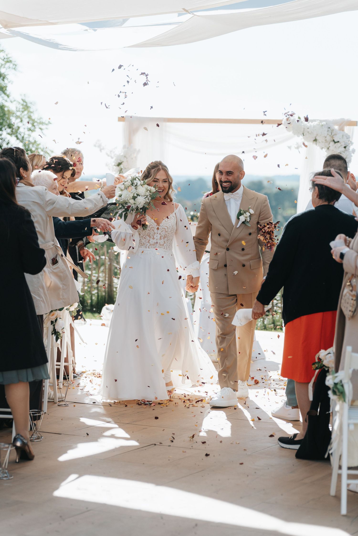Wedding guests celebrate with confetti and dancing in a sun-filled reception venue during a joyous celebration.