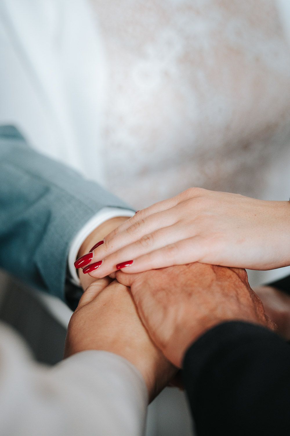 Close-up shot of two people holding hands tenderly against a soft white and gray background showing support and comfort.