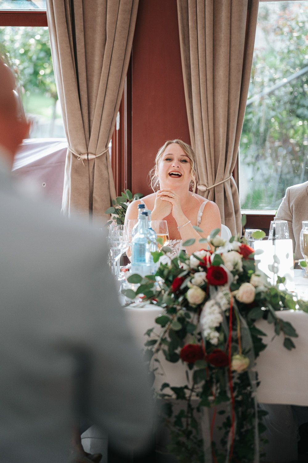 A joyful moment captured during a wedding reception, with elegant floral centerpiece and draped curtains in the background.