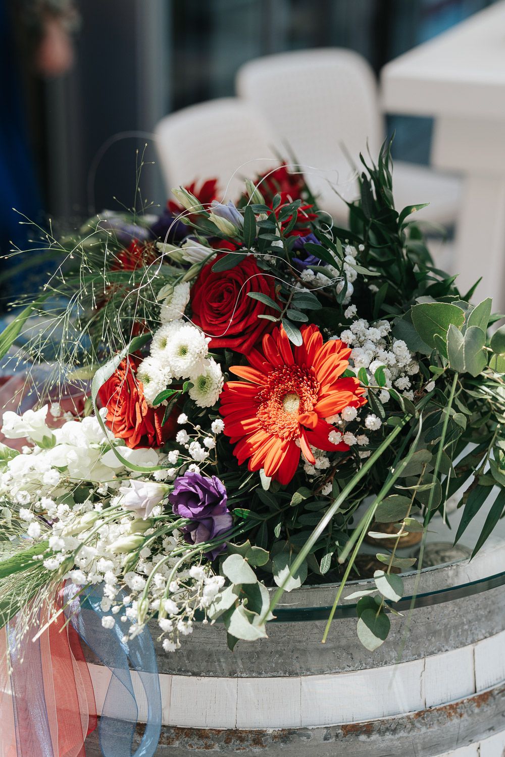 Floral arrangements featuring red gerbera daisies, white baby's breath, and greenery displayed in curved stone containers.