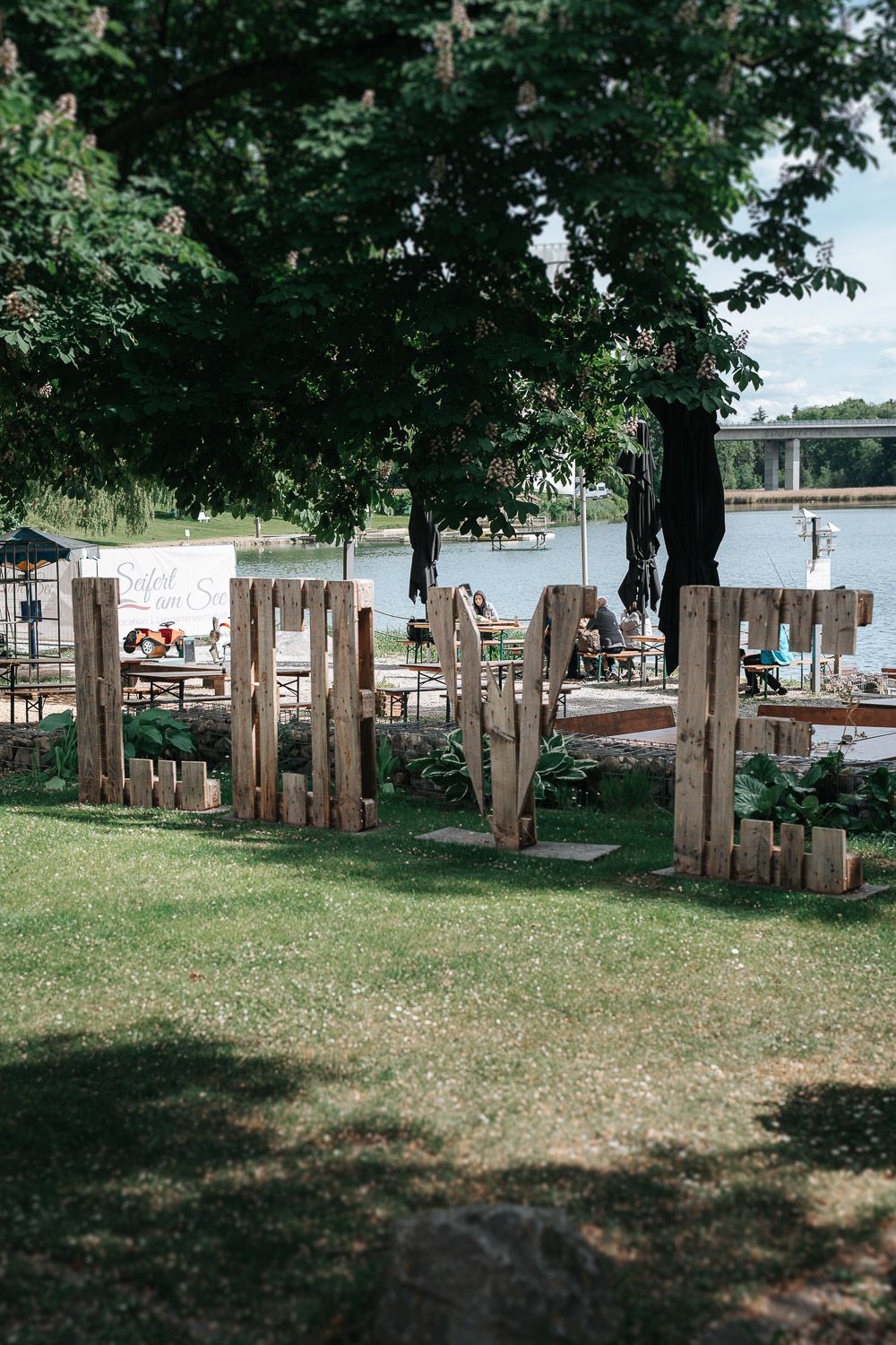 Wooden dock and seating area overlooking a river on a sunny summer day with trees providing shade.