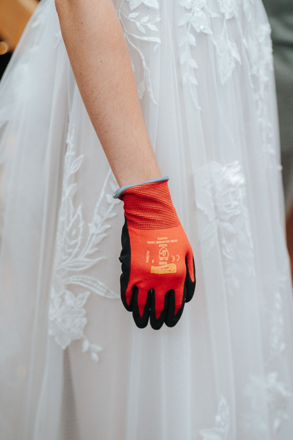 A white wedding dress adorned with lace details and a contrasting red work glove with black trim.