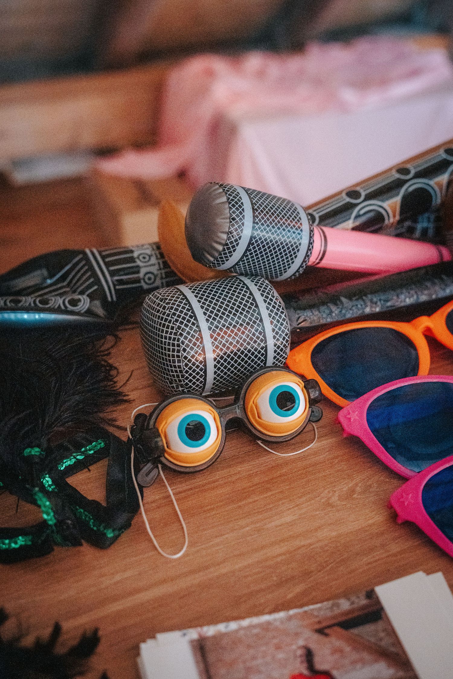 Photo booth props on a wooden table, including inflatable microphones, googly eye glasses, colorful sunglasses and a feather mask.