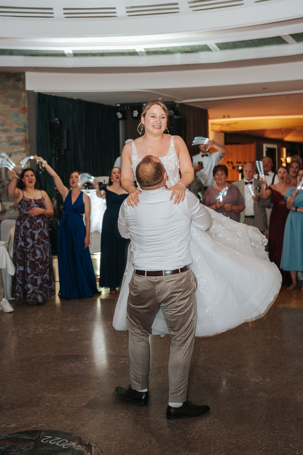 Two people perform an elegant dance lift during a wedding reception as guests watch in a circular venue.