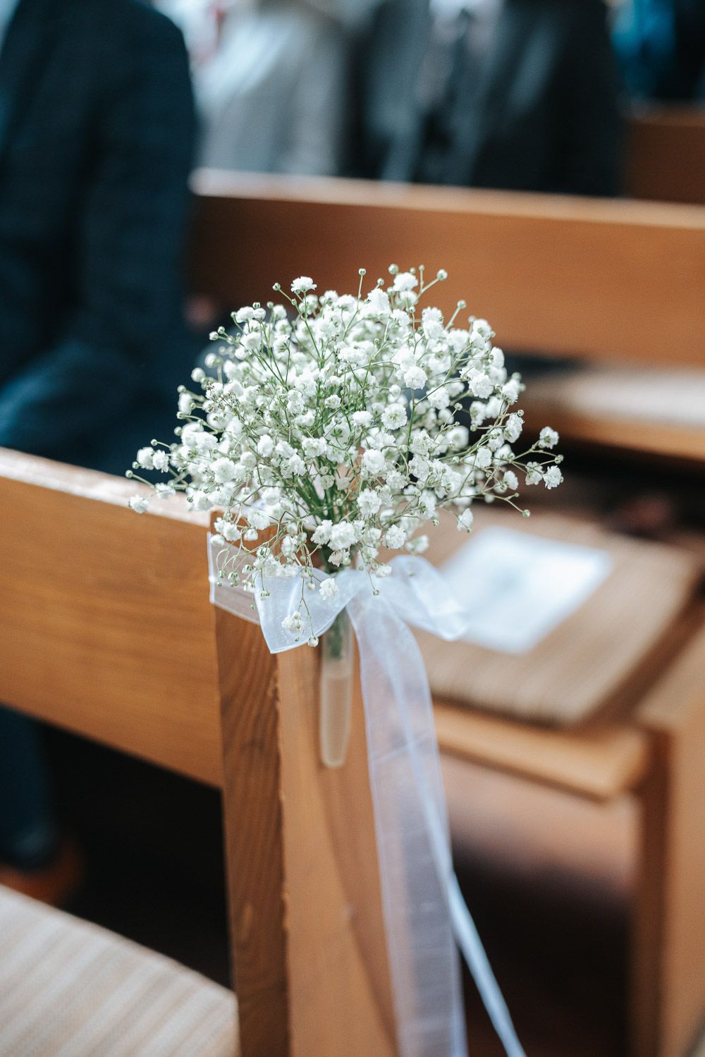 Baby's breath flowers tied with white ribbon decorate wooden pews in a church aisle for a wedding ceremony.