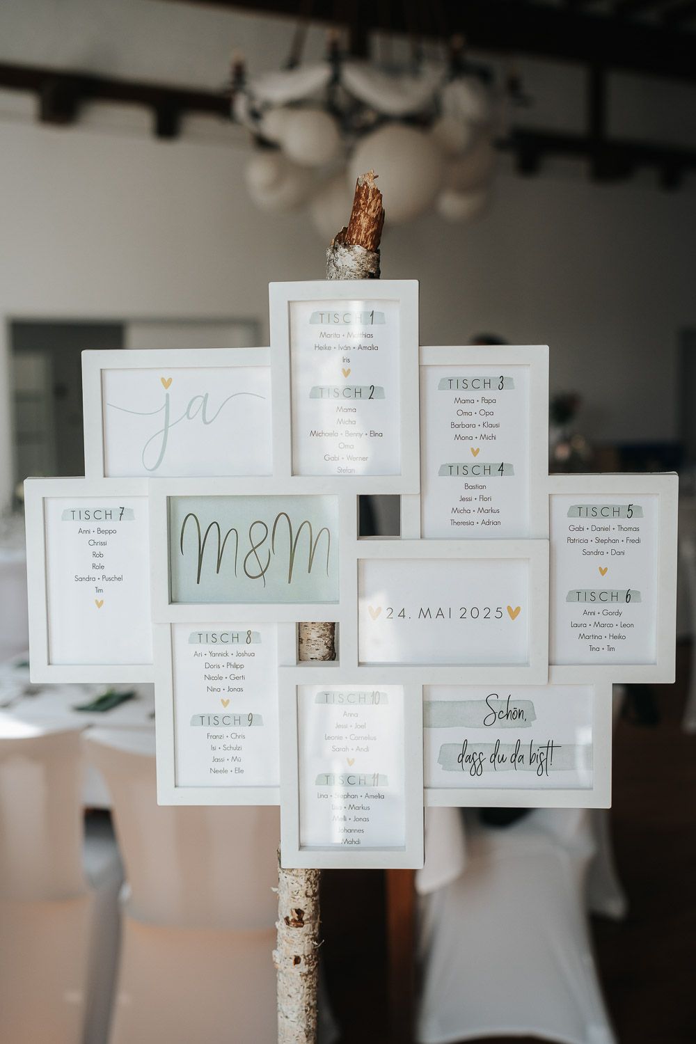 A modern wedding seating chart displayed on white paper cards arranged in a geometric pattern on a birch pole stand.