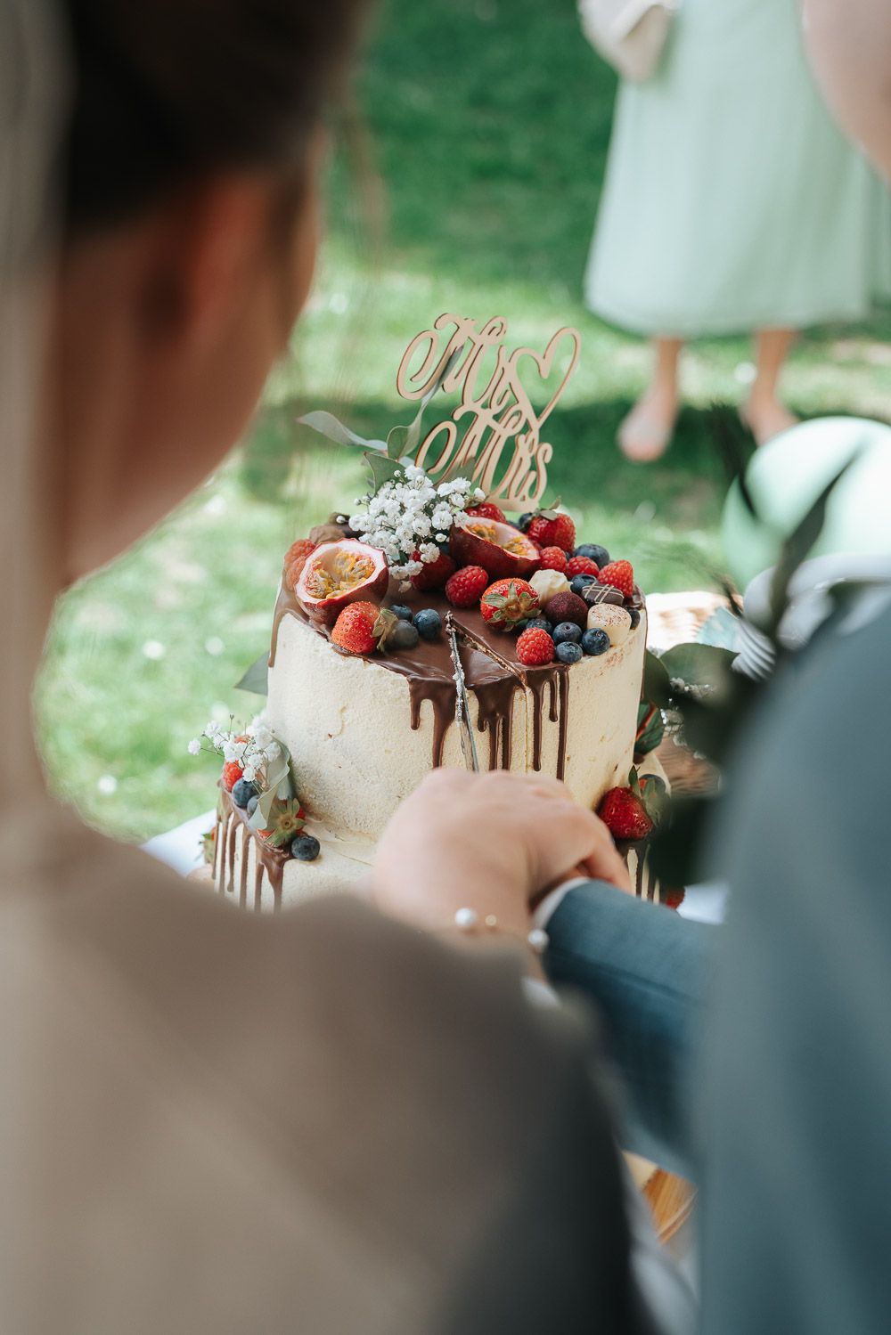 Beautiful chocolate drip cake decorated with fresh berries and chocolate treats on a cake stand at a party.