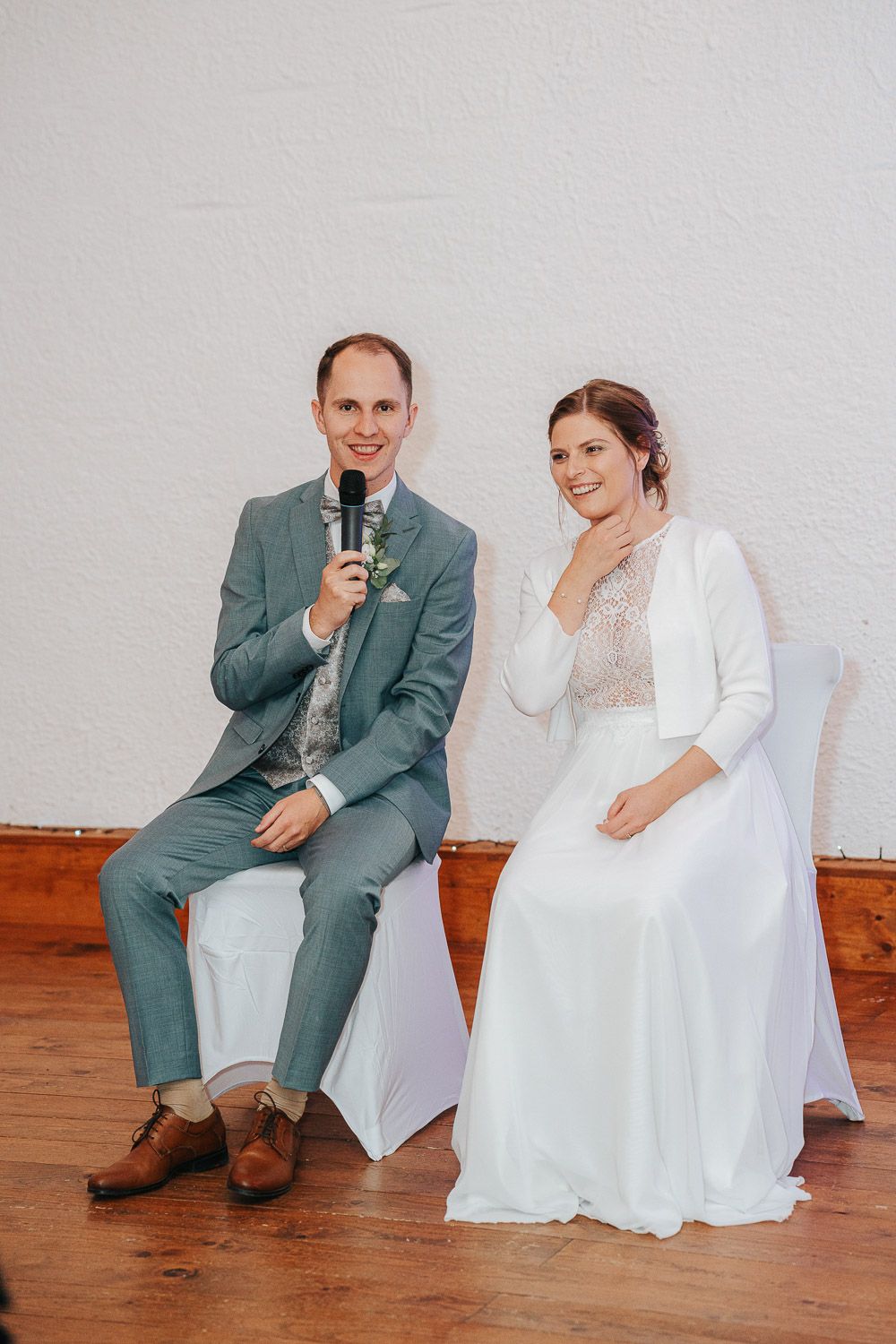 Four candid wedding photos showing a couple sitting together on a wooden floor and sharing joyful laughter.