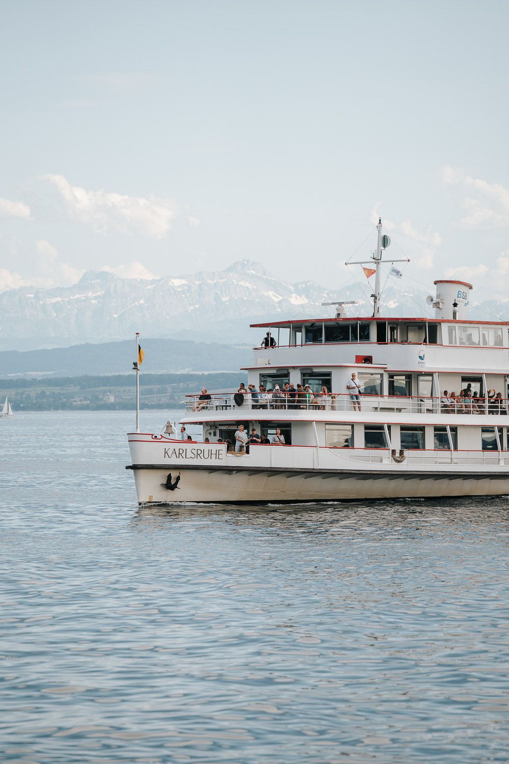 Tourist ferry boat cruises on Lake Constance with snow-capped Alps mountains visible in the background.