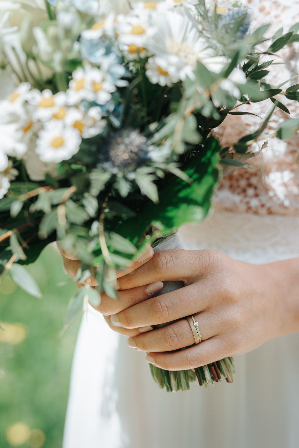 Hand holding delicate white daisies in a wedding bouquet with an engagement ring visible on finger.