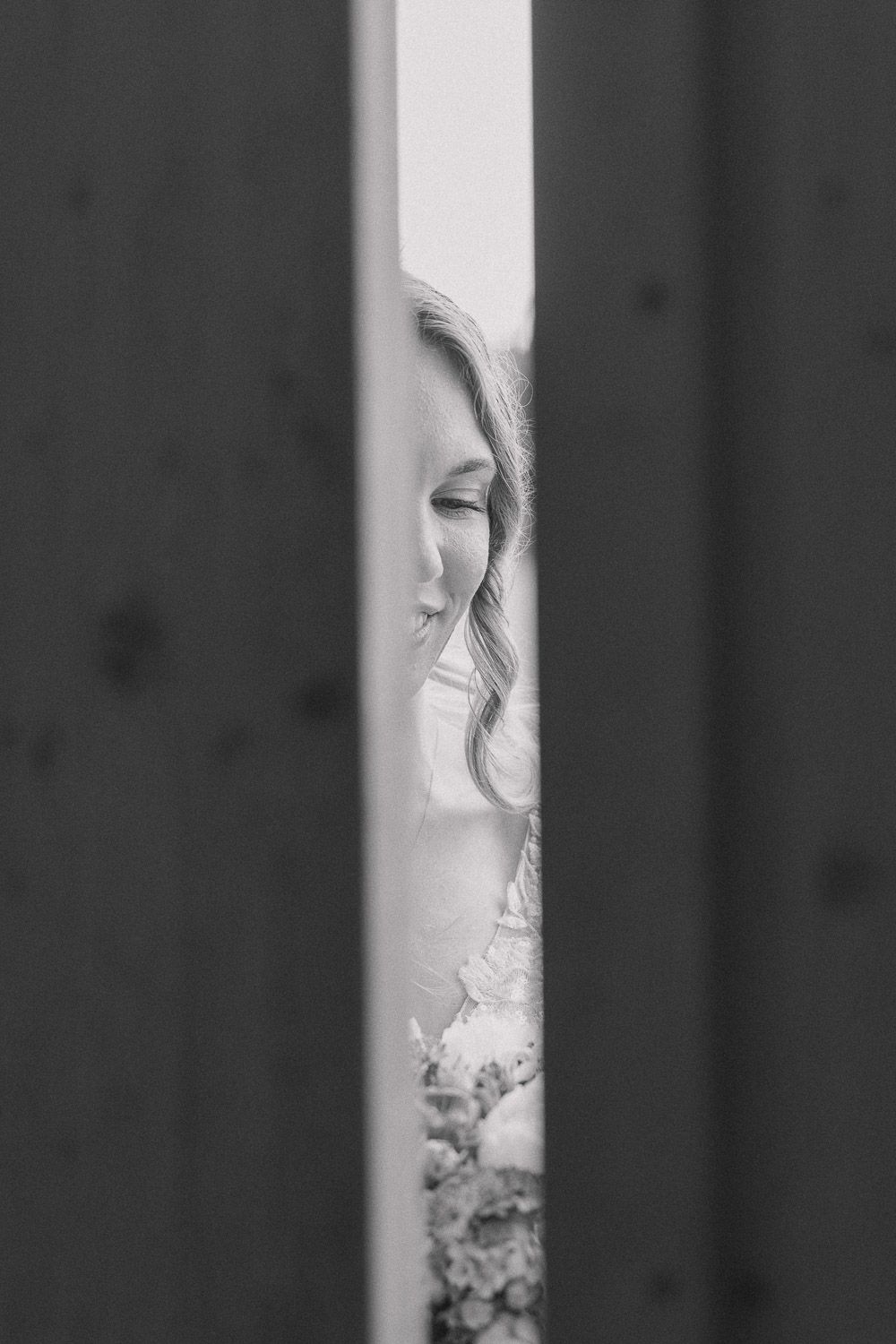 Black and white artistic portrait through vertical wooden slats creates a dramatic framing effect.