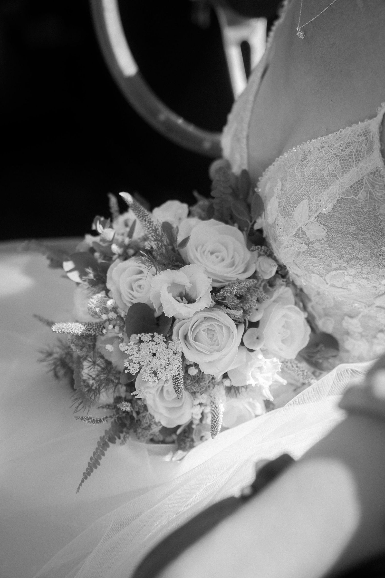Black and white photo of a bridal bouquet with roses resting against a lace wedding dress.