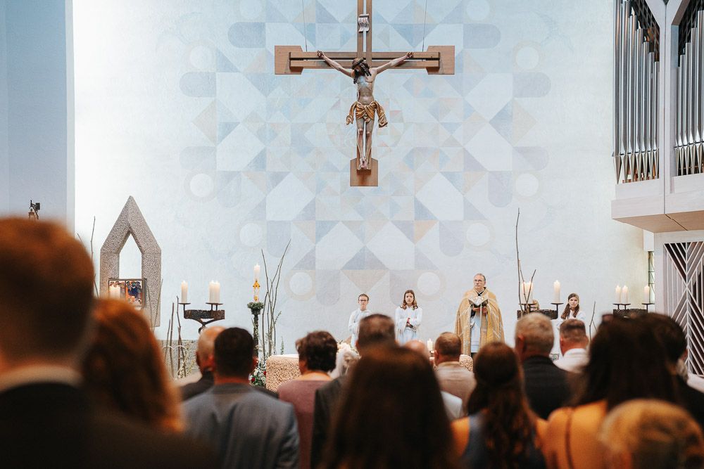 A congregation gathers in a church sanctuary during a service with a large crucifix mounted on the wall behind the altar.