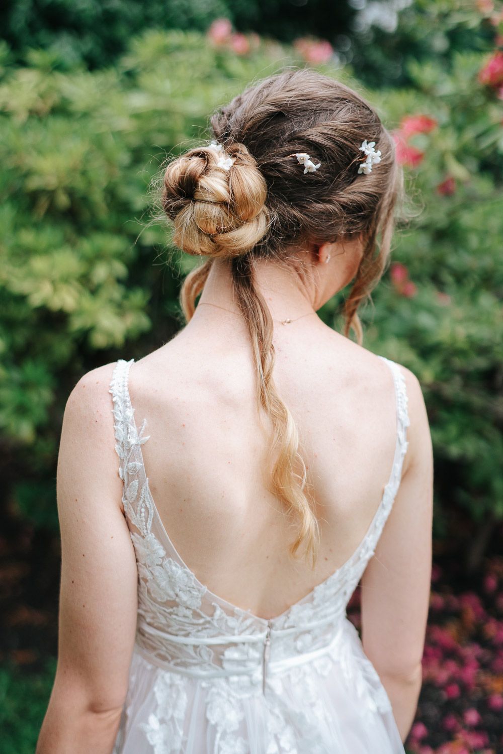 A romantic bridal hairstyle with loose curls and floral accents shown from behind in a lace wedding dress.