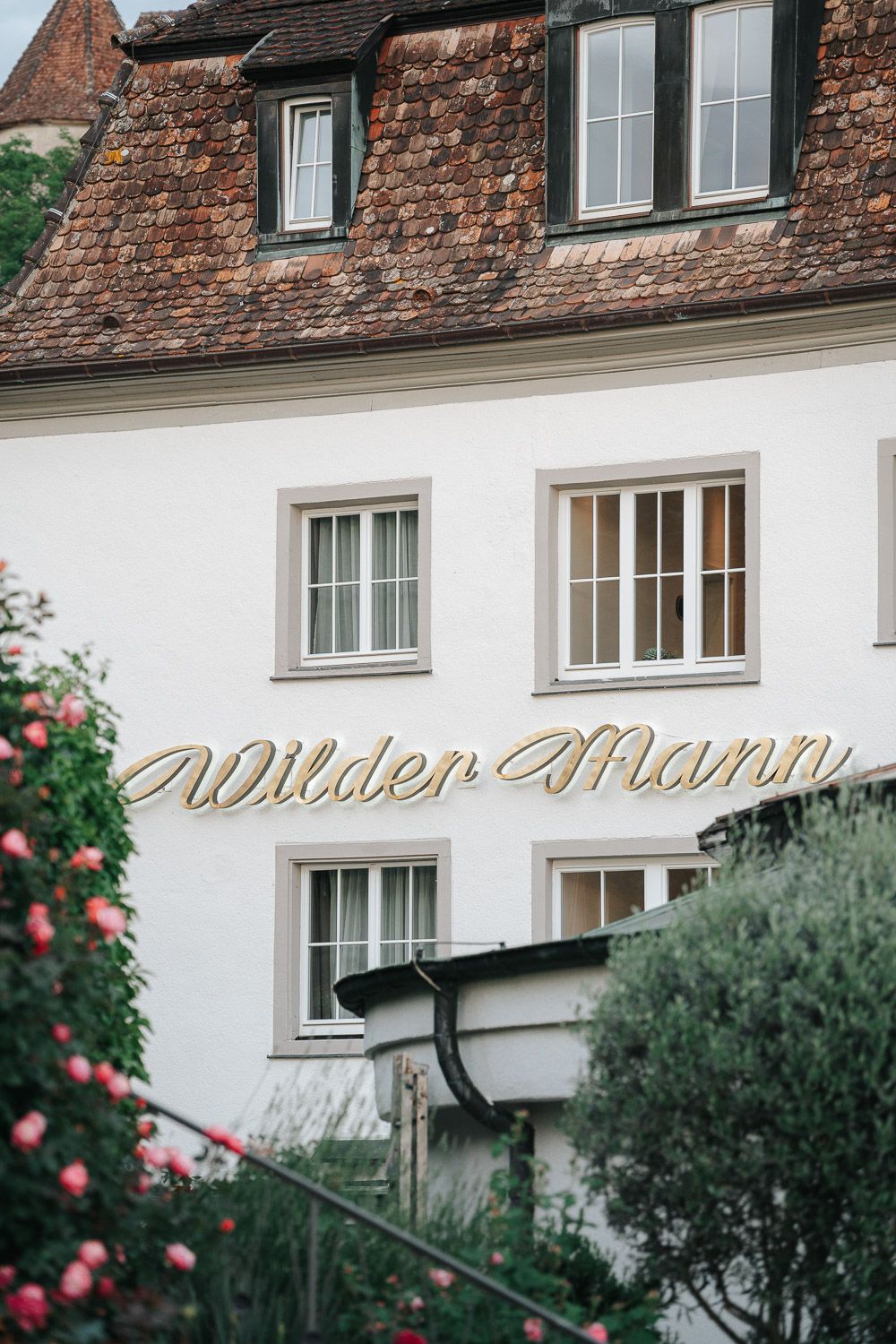 Rustic white building facade with red brick upper wall and elegant script text signage against a natural background.