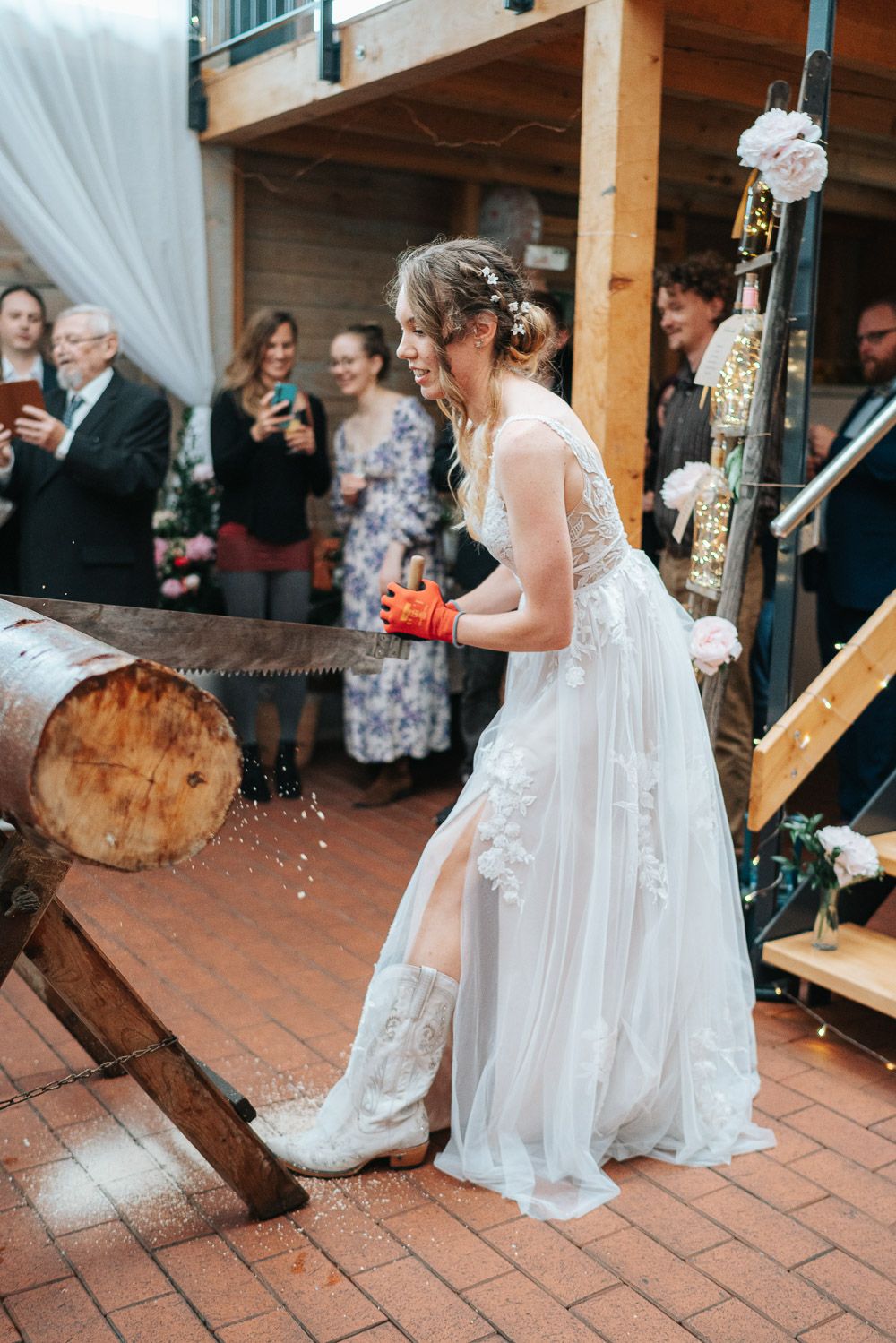 A person in a flowing white lace wedding dress stands on brick patio during an outdoor wedding reception celebration.