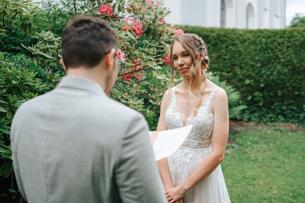 A beautiful outdoor wedding ceremony takes place in front of a garden with red roses and green hedges.