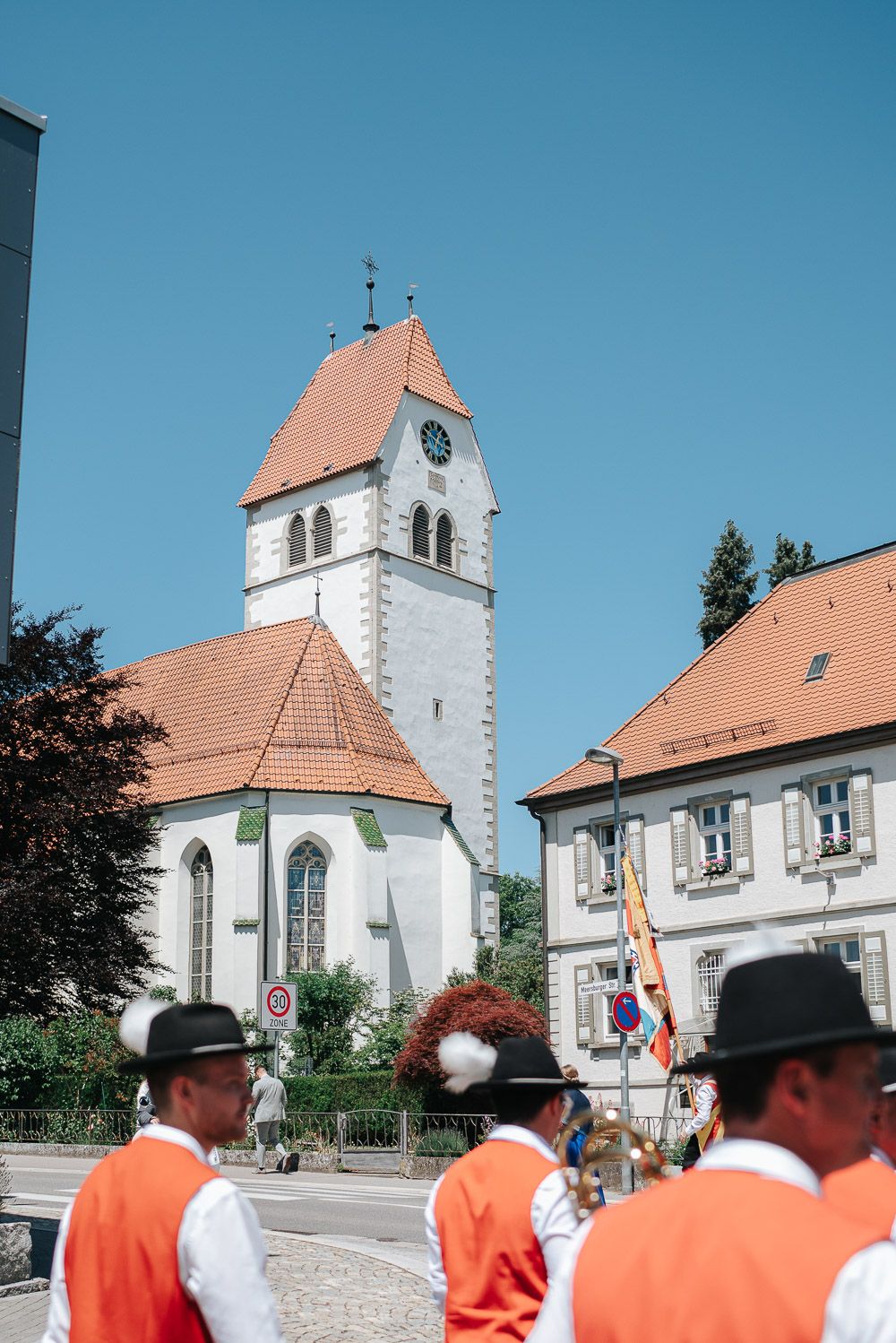 White church building with orange tiled roof against blue sky as people in orange shirts gather in foreground.