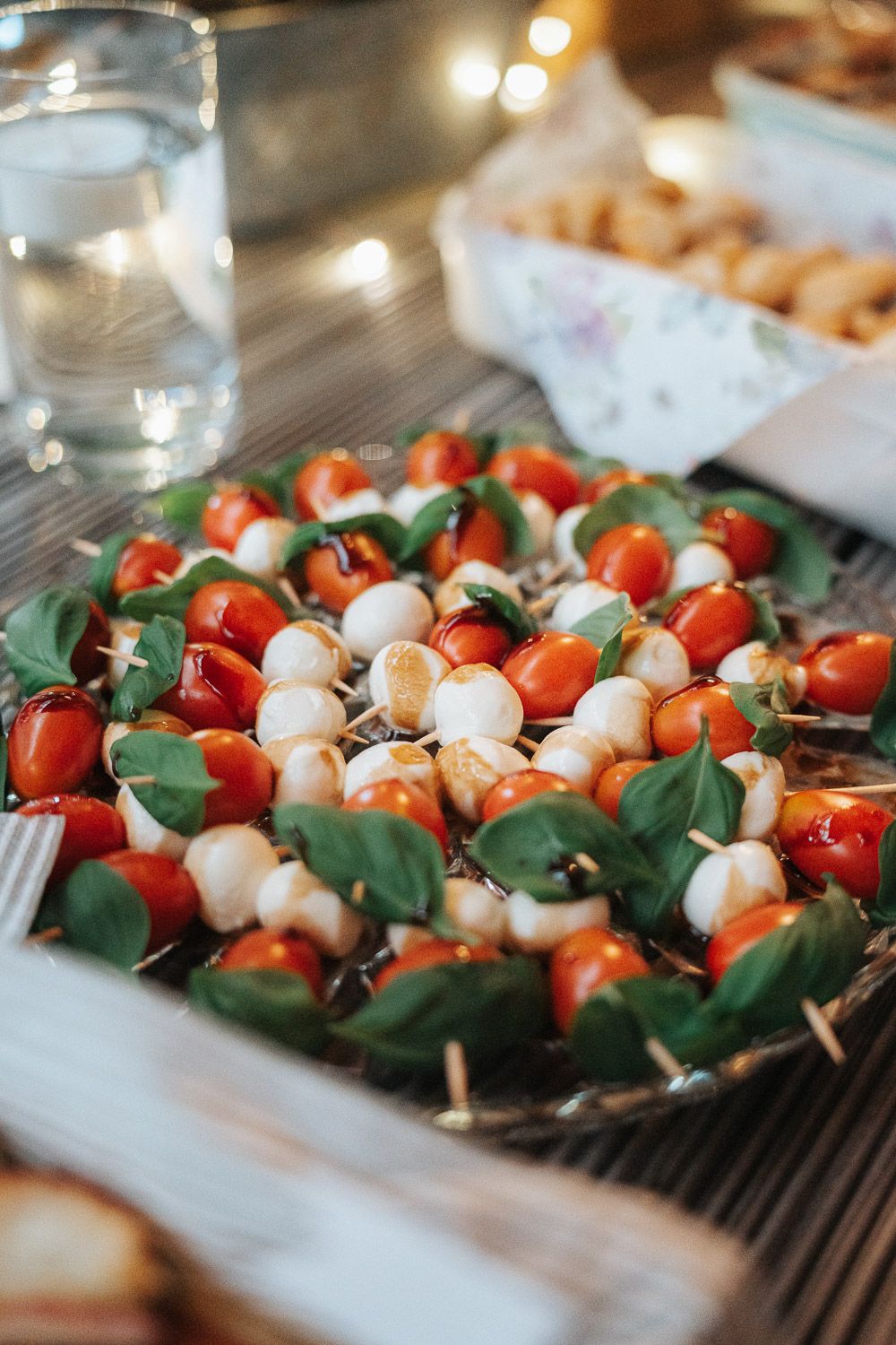 Fresh caprese appetizers with cherry tomatoes, mozzarella balls and basil leaves arranged on serving platter.