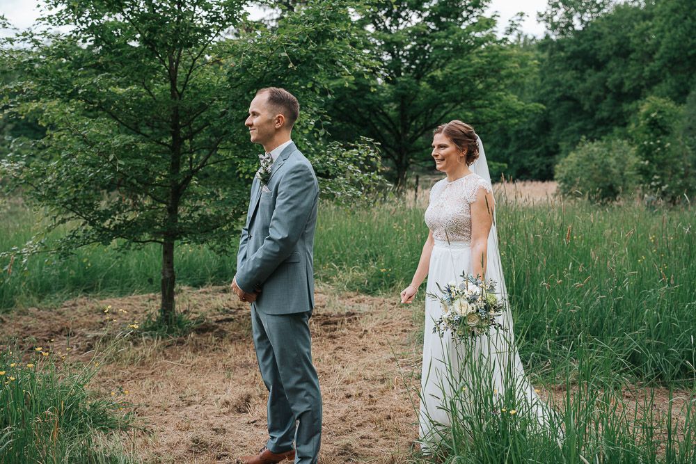 A couple shares an intimate moment outdoors surrounded by lush green trees at their garden wedding celebration.