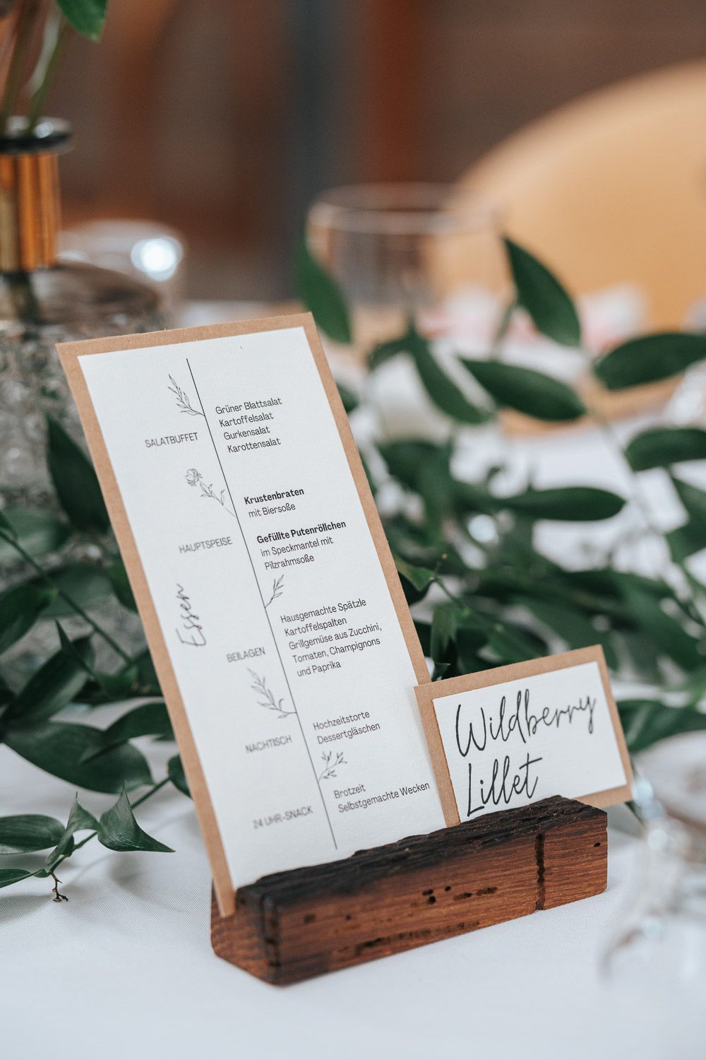 A series of rustic wooden table card holders displaying wedding seating charts with greenery accents and white linens.