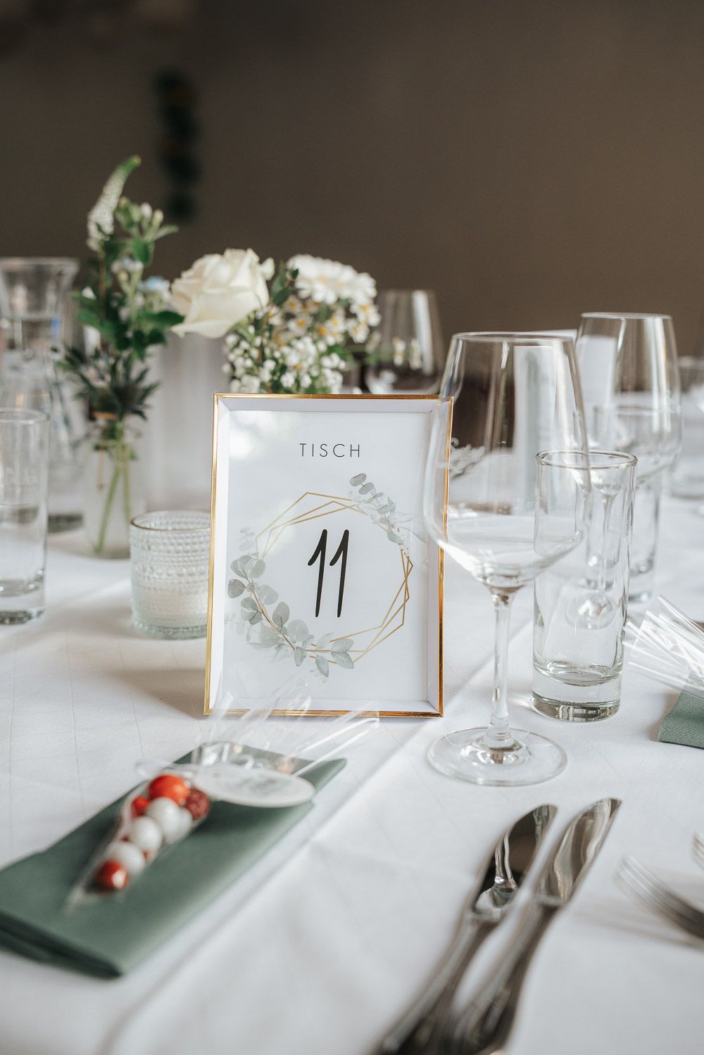 Elegant wedding table setting with table number 11 in gold frame, wine glasses, and white floral centerpieces.