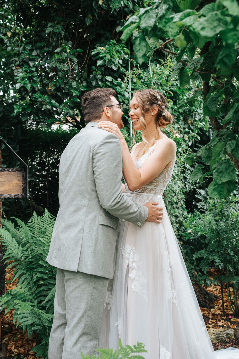 A tender wedding moment captured in a garden surrounded by green leaves and ferns.