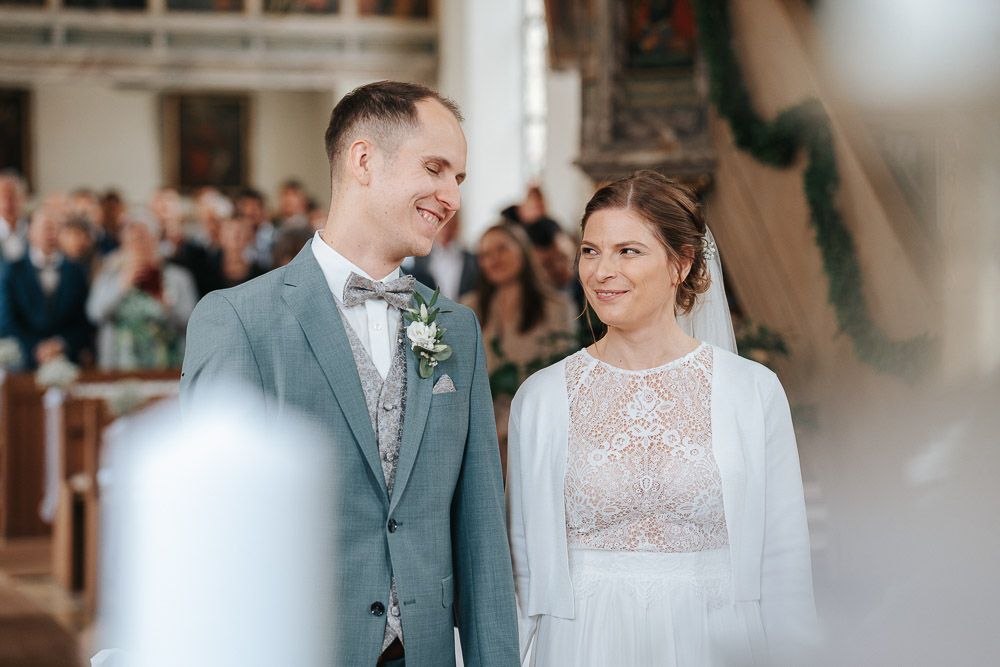 A couple shares a joyful moment during their wedding ceremony in an elegant, light-filled indoor setting.
