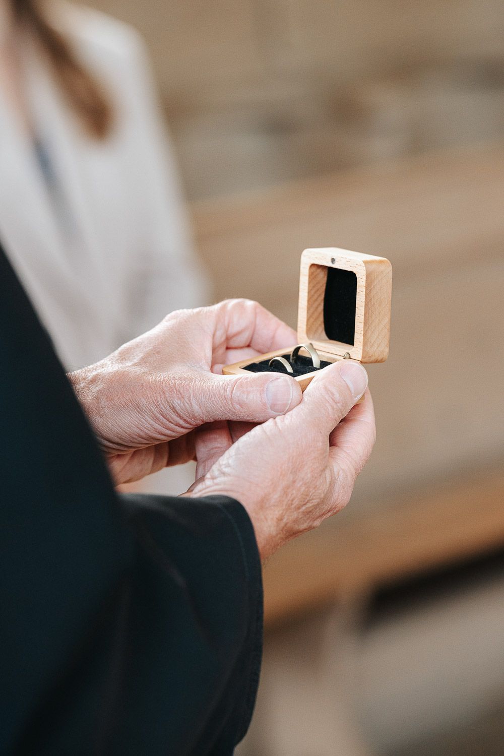 Hands hold a small wooden box containing a ring during an intimate moment.
