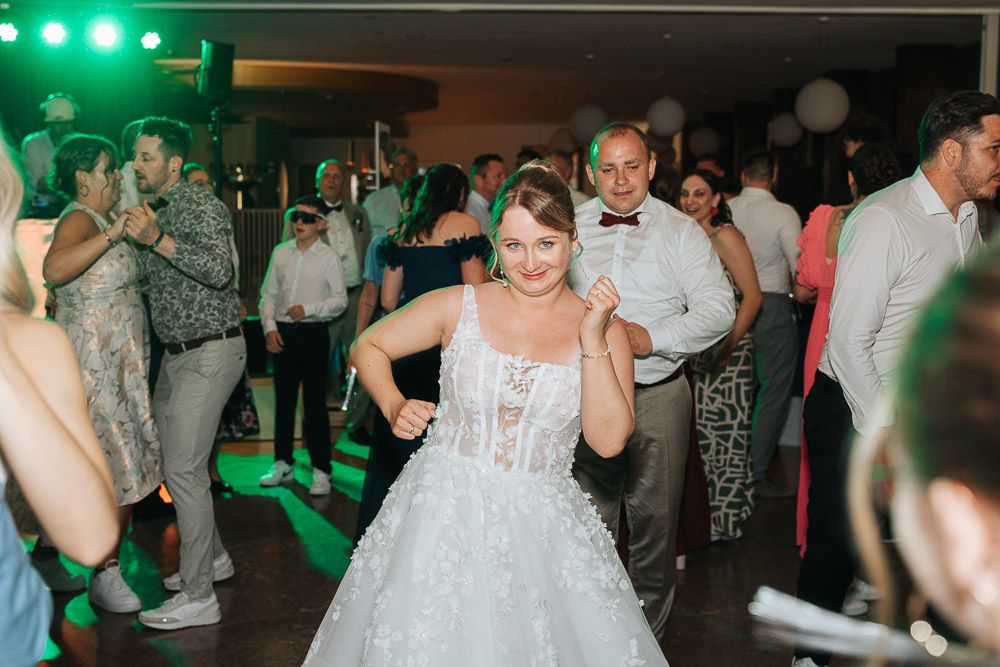 Wedding reception dance floor filled with guests under green party lighting in an elegant venue.