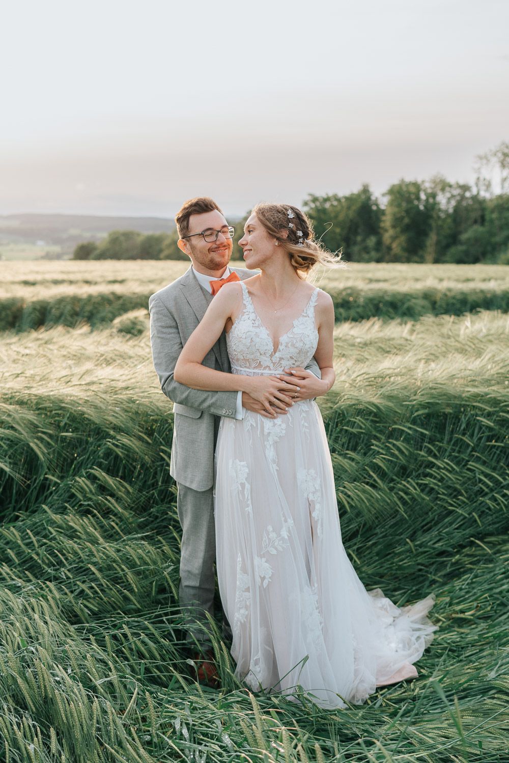 A romantic wedding couple embraces in a scenic field of tall grass during golden hour.
