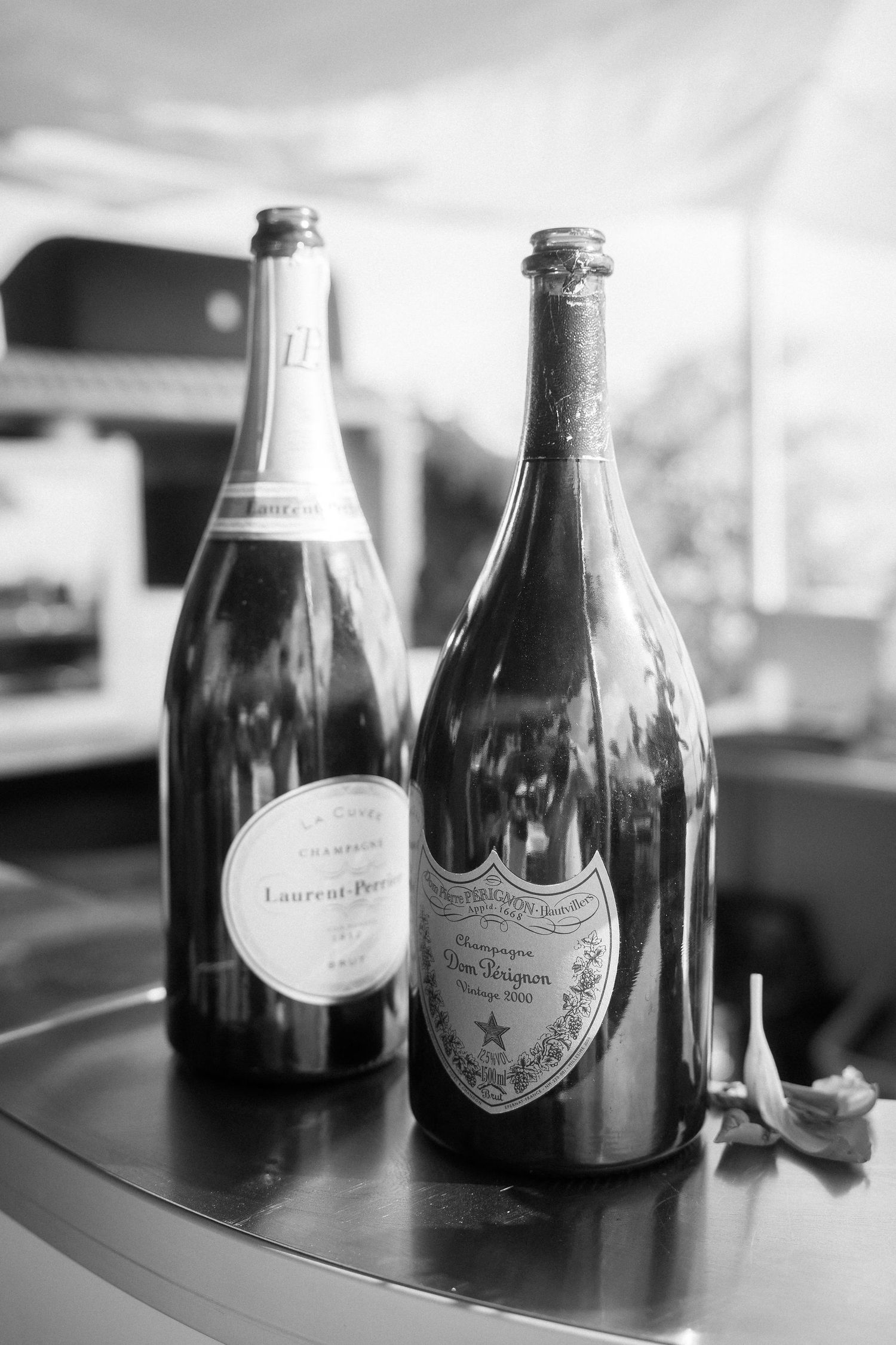 Black and white photo of two empty Laurent-Perrier and Dom Pérignon champagne bottles standing on a curved bar counter.
