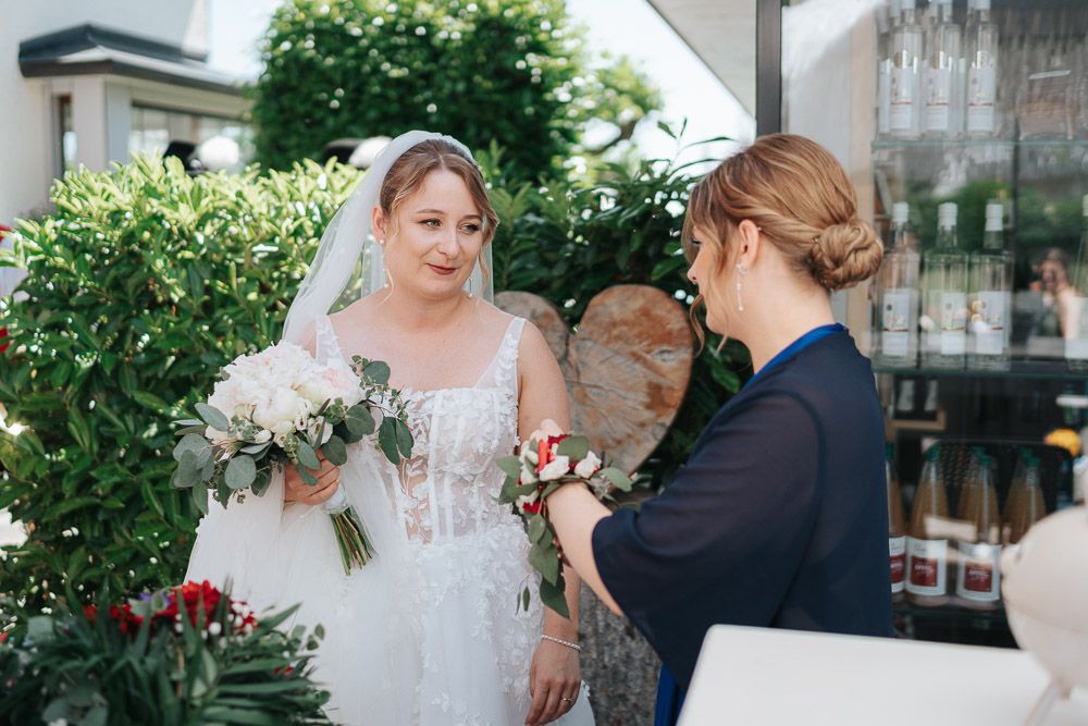 A wedding couple embraces in a romantic outdoor garden setting surrounded by lush greenery and flowers.