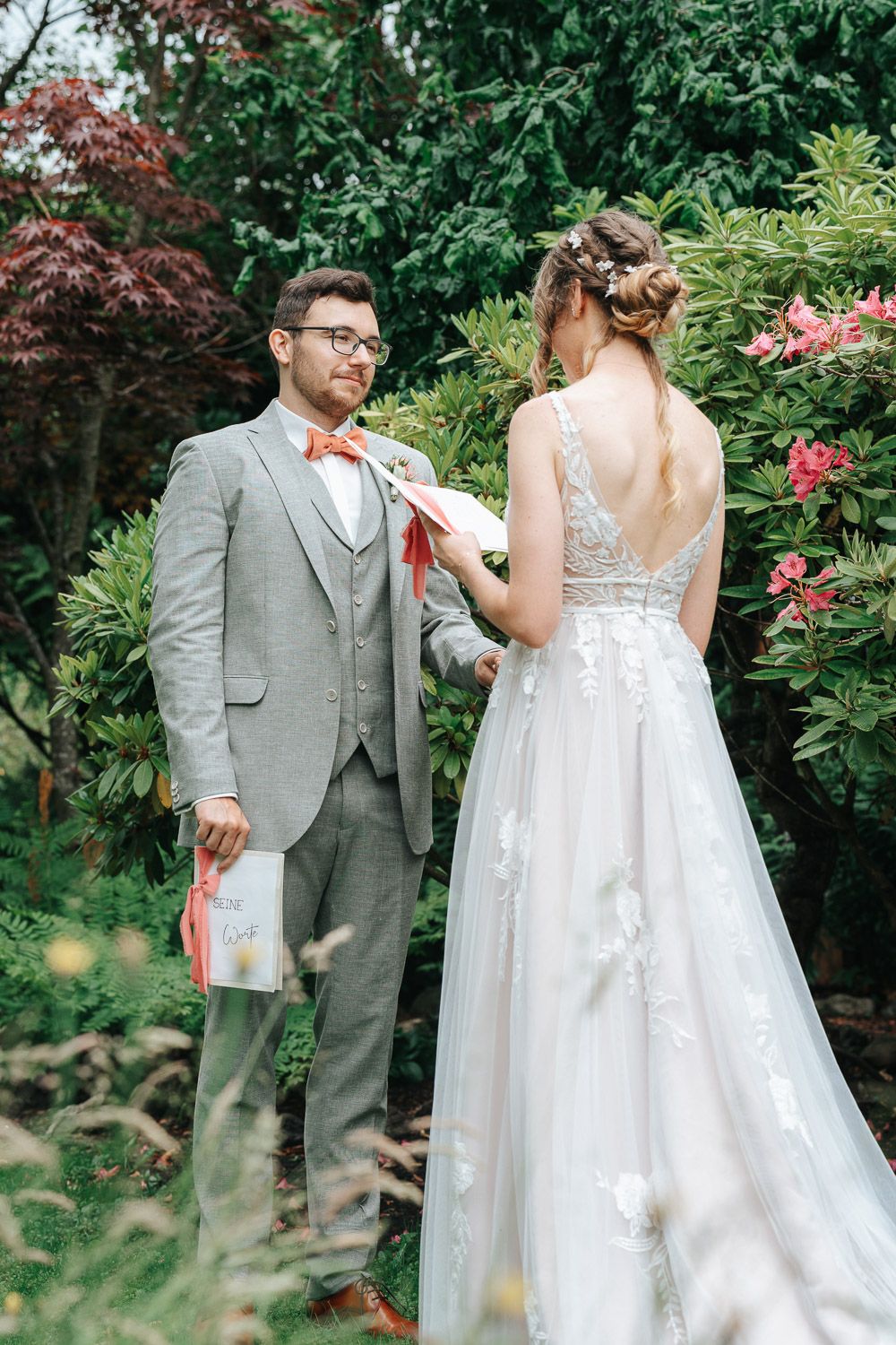 Bride and groom share a charming moment together in a garden setting with blooming flowers and trees.