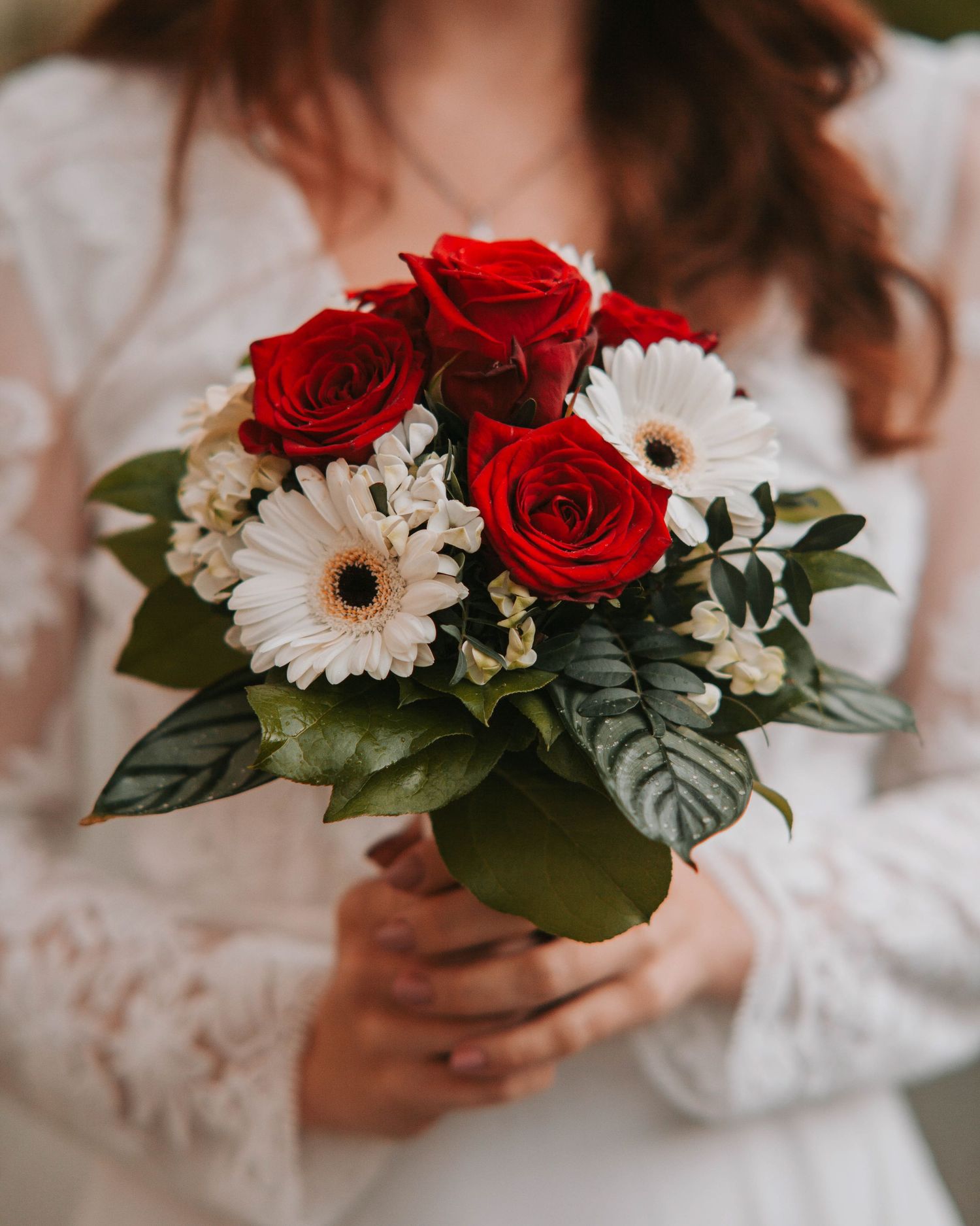 A romantic bouquet of red roses and white daisies held against a white lace dress background.