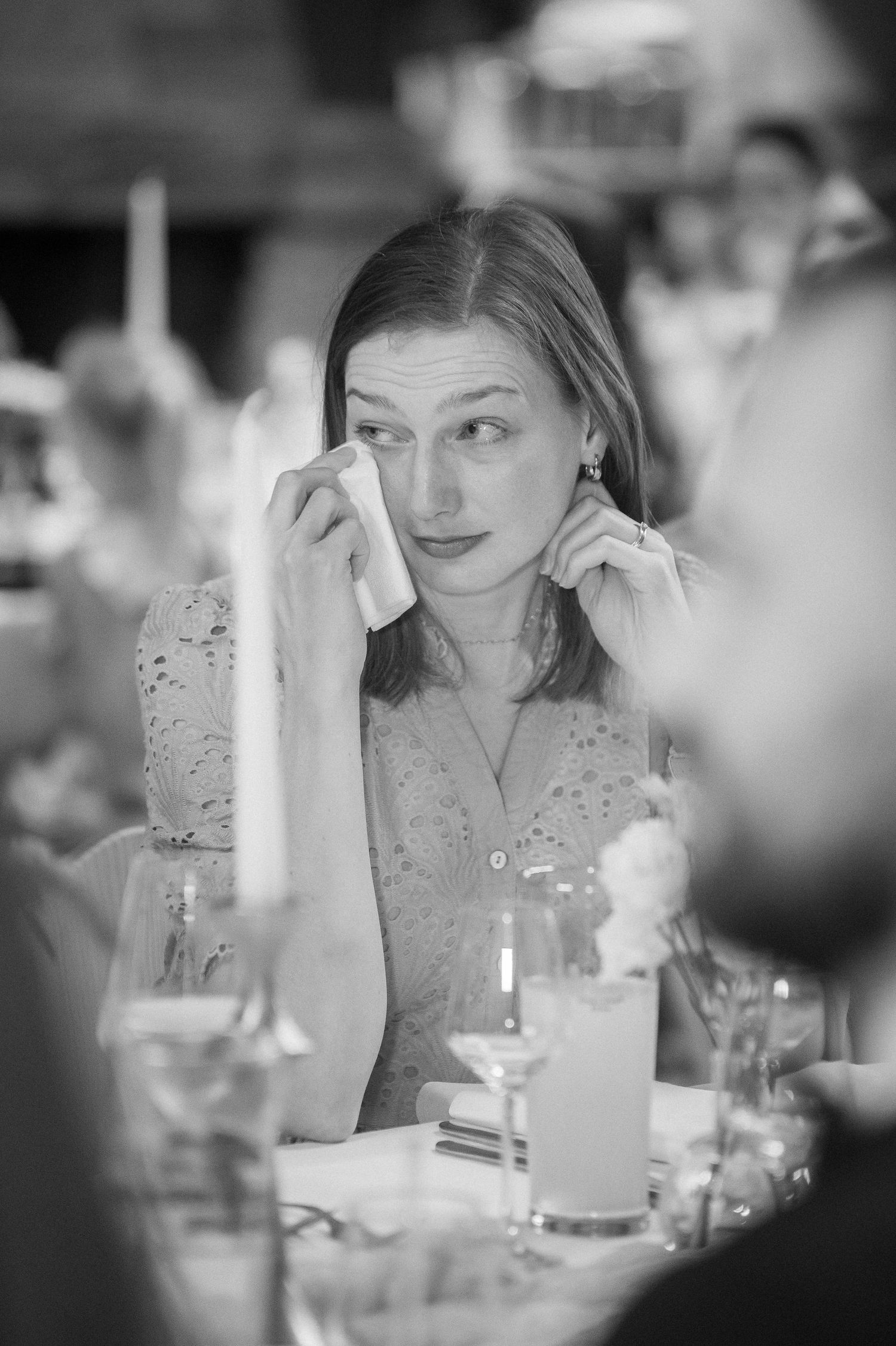 Black and white photo of a woman dabbing her eyes with a tissue at a candlelit dinner table during an emotional wedding reception.