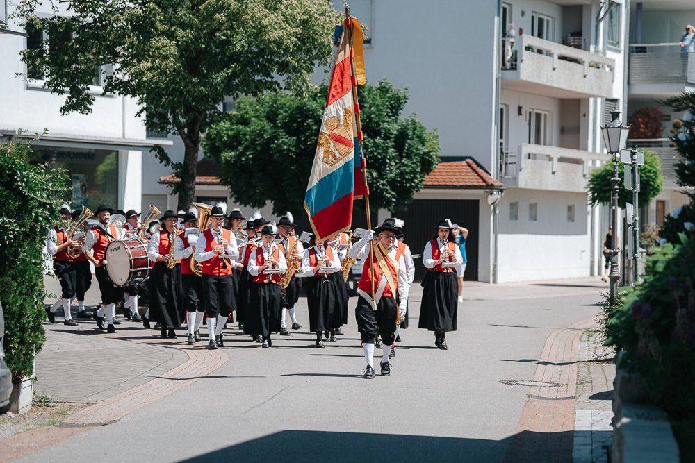 A row of senior citizens riding mobility scooters in single file formation along a residential street during a parade.