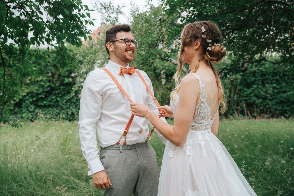 A couple in wedding attire share a joyful outdoor moment in a lush green garden setting.