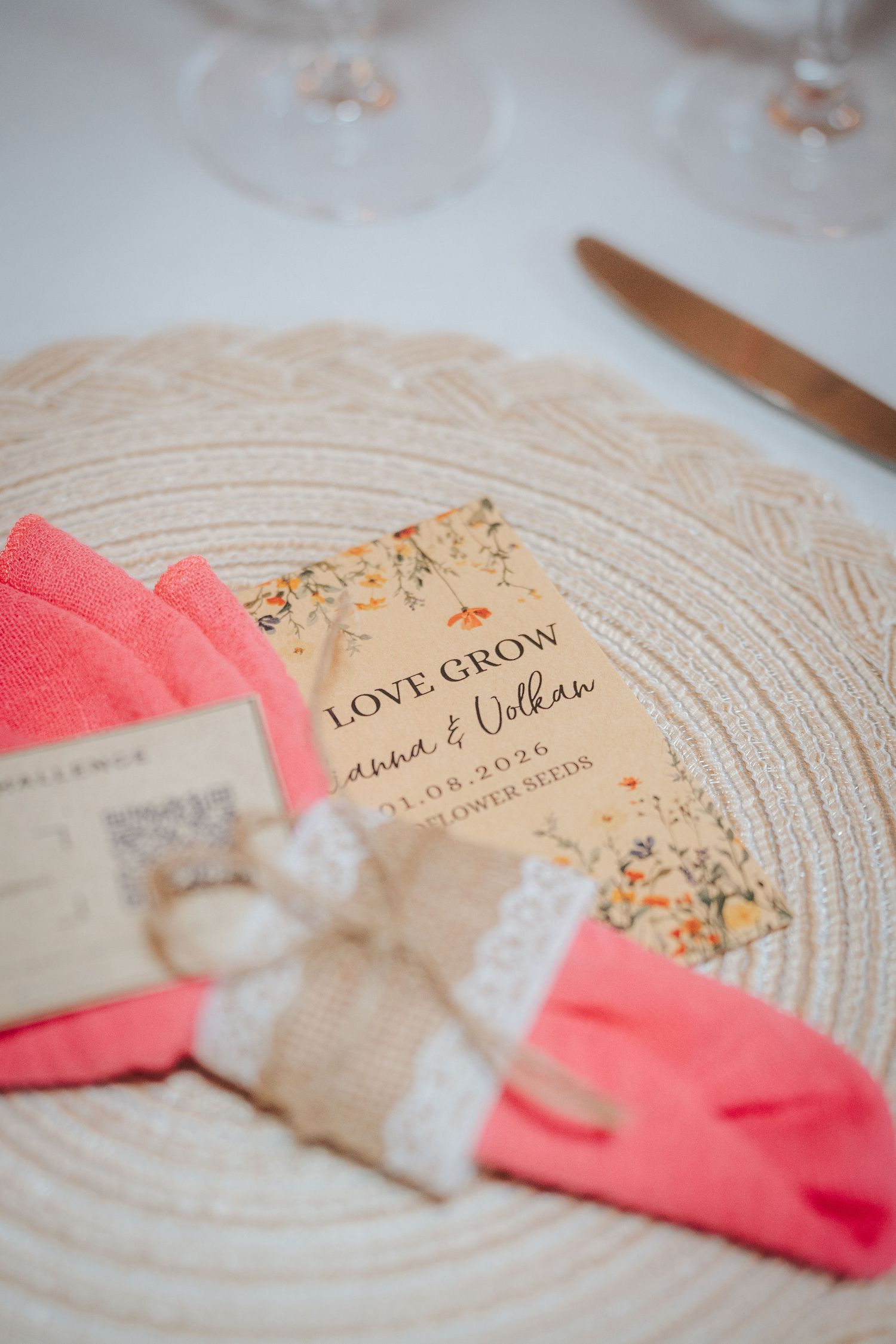 Wedding place setting with a coral napkin tied in burlap and lace, topped by a floral Love Grow wildflower seeds favor card.