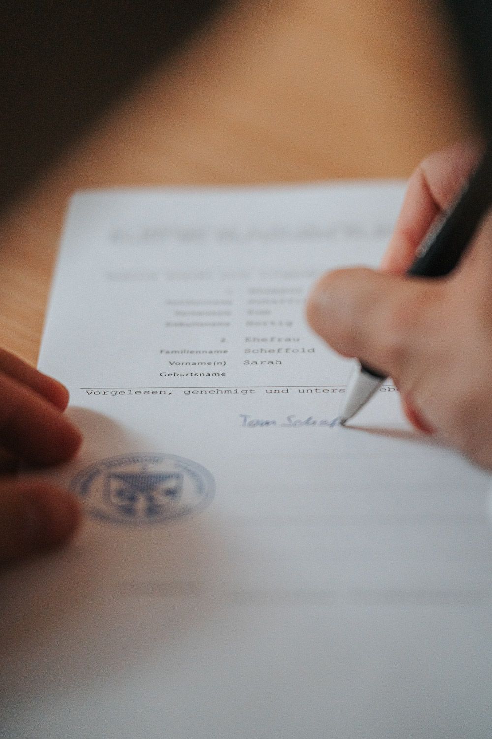 A hand signs important documents with a pen while an official seal and signature marks the paper below.