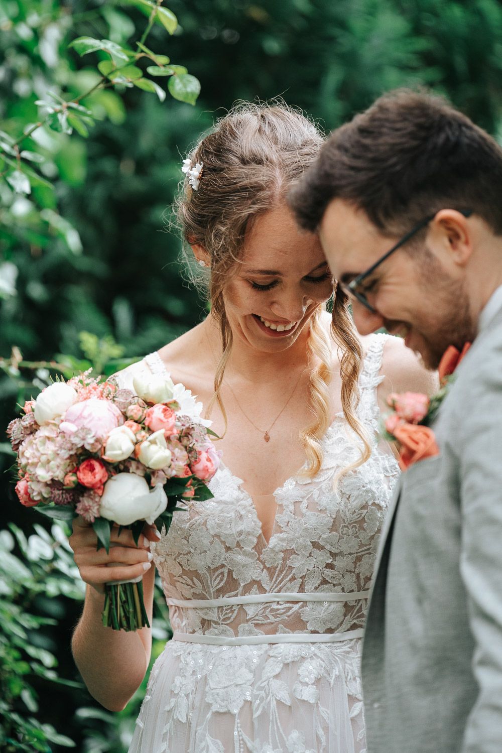 A couple shares an intimate moment outdoors while the bride holds a pink and white floral wedding bouquet.