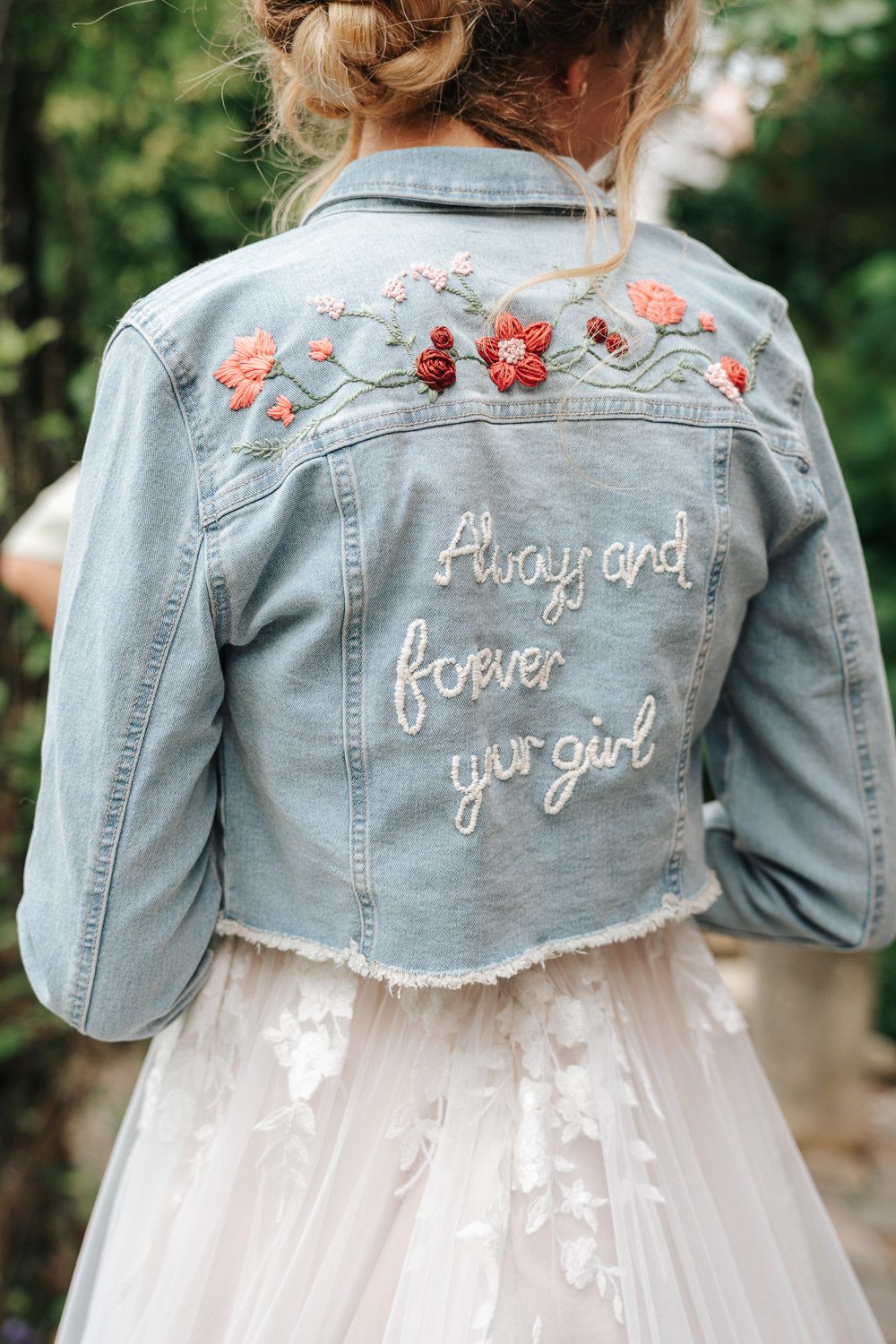 Light denim jacket with floral embroidery and 'always and forever your girl' text worn over white tulle wedding dress.