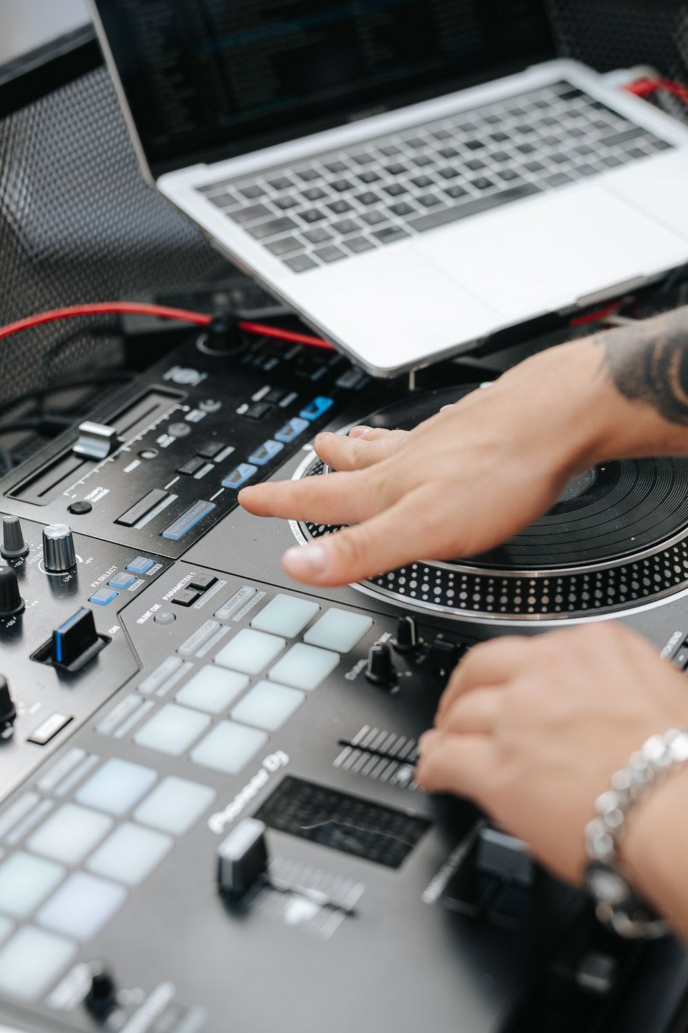 DJ mixing music at turntables with laptop and digital controller deck showing hands adjusting controls and faders.