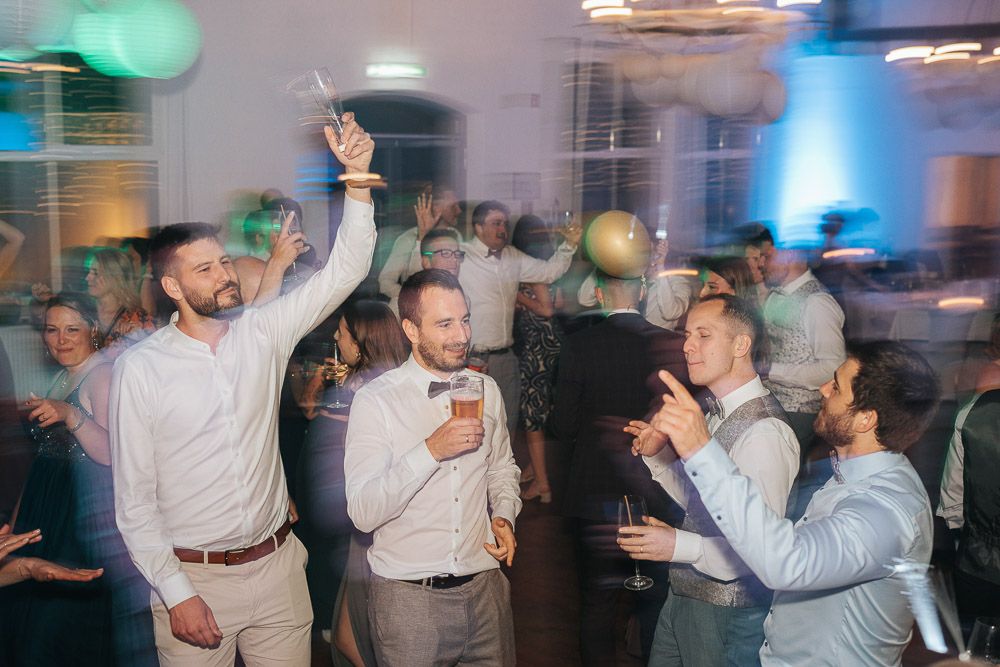 Party guests dancing and celebrating at an indoor event with colorful lighting and festive atmosphere.