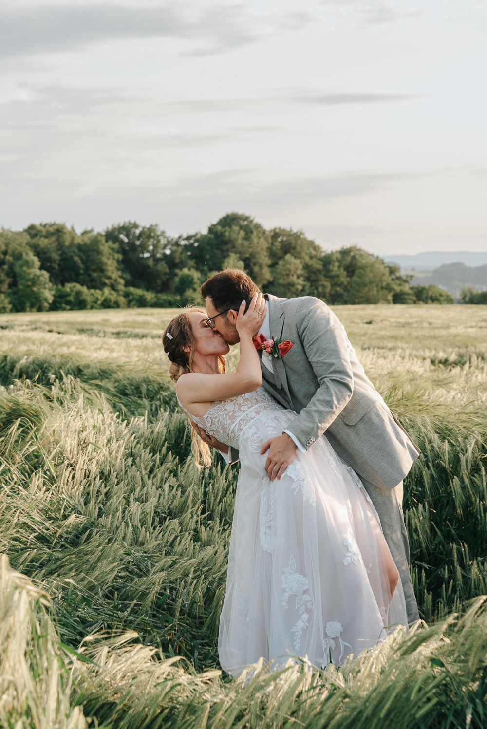 A romantic wedding couple shares tender kisses in a serene golden wheat field during a summer photo session.