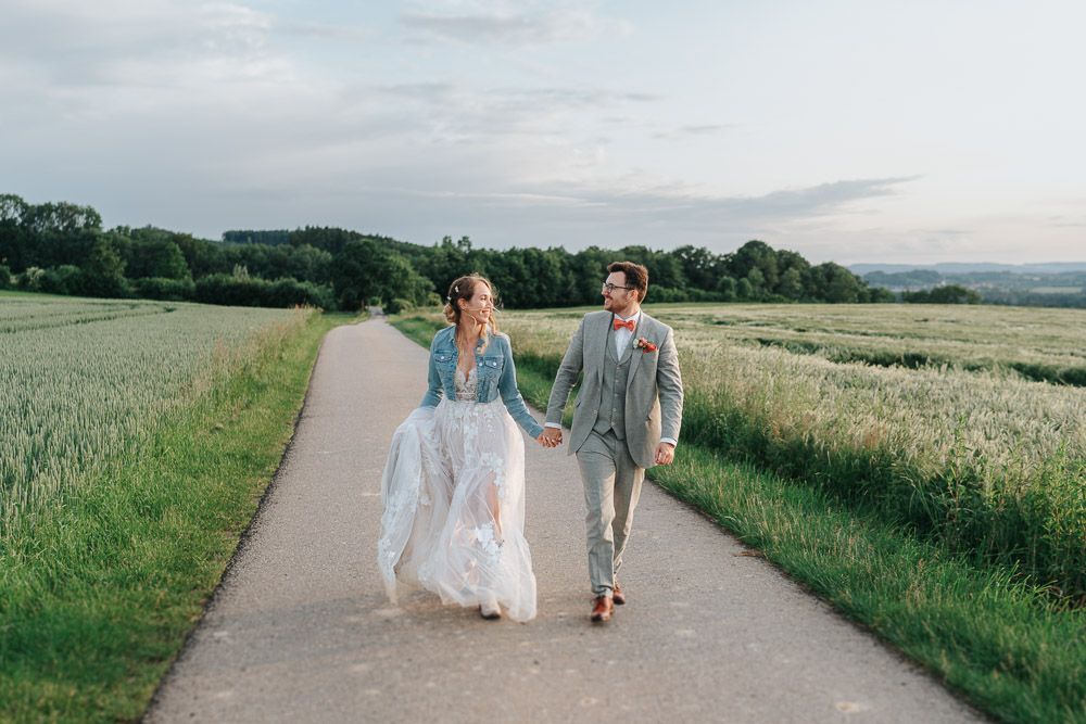 A couple strolls along a scenic path through rolling green meadows and wildflower fields on a summer afternoon.