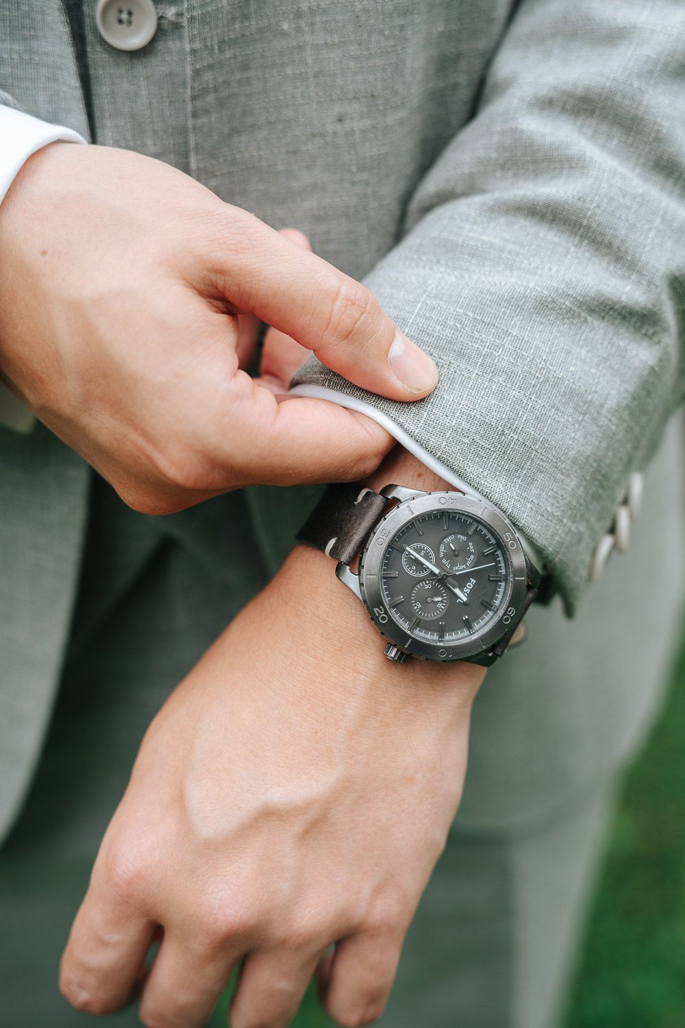 A series of close-up shots showing a black watch being put on a wrist against a gray suit sleeve background.