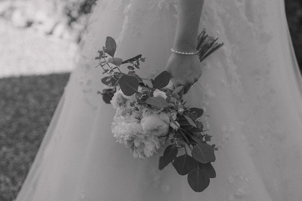 Black and white photograph of a wedding bouquet lying against a white dress.